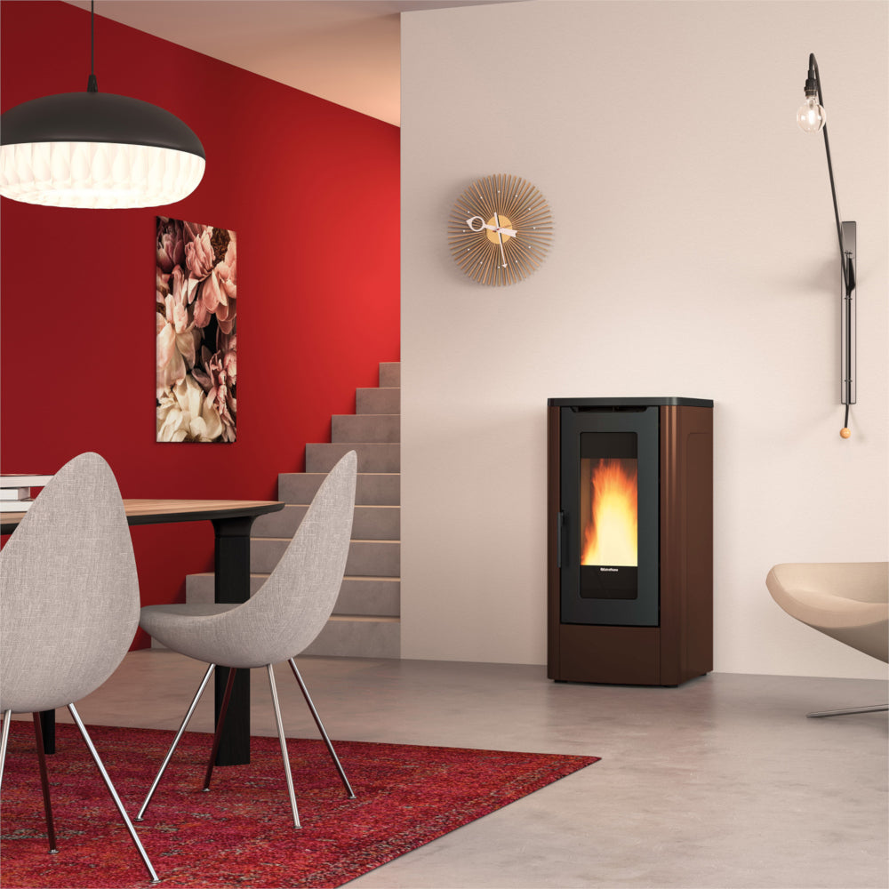 Ambientebild: Extraflame kanalisierter Pelletofen DAHIANA PLUS 5.0 EVO in Bronze, im Wohnzimmer neben Treppe roter Wand Tisch Stuehlen | Klimaworld.com
