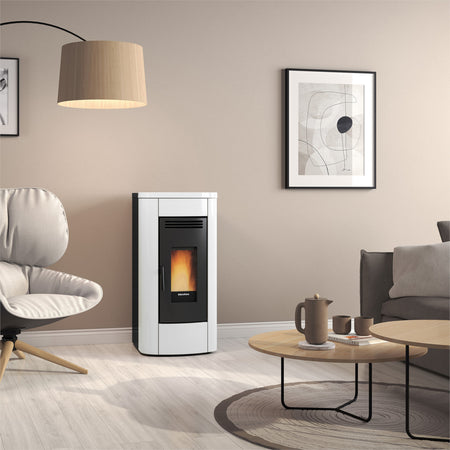 Ambientebild: Extraflame beluefteter Pelletofen KLAUDIA 5.0 EVO weiss-schwarz mit Flamme im Glas im Wohnzimmer neben Sessel | Klimaworld.com
