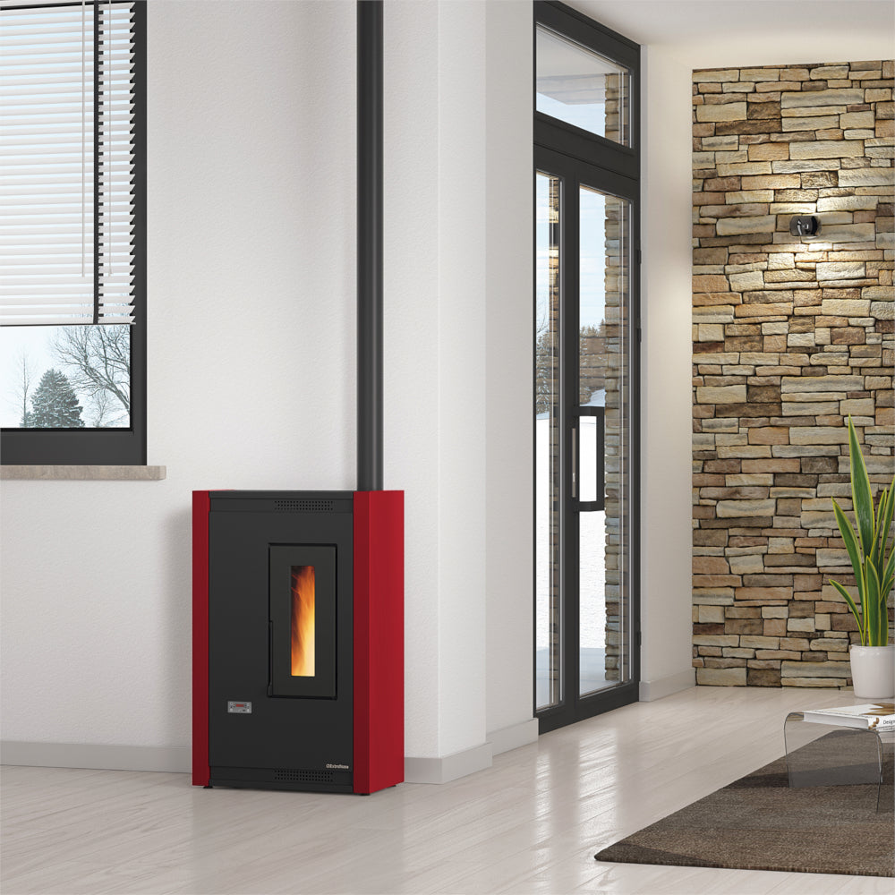 Ambientebild: schmaler Extraflame beluefteter Pelletofen LUISELLA 5.0 in Wohnraum mit Steinwand, Fenster, schwarz-roter Korpus | Klimaworld.com