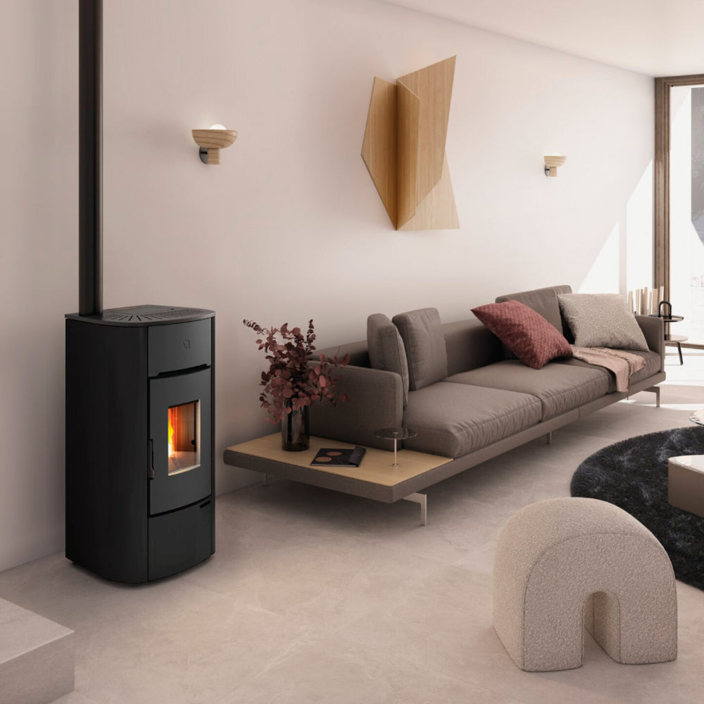 Extraflame kanalisierter Pelletofen MARIELLA PLUS Schwarz im Wohnraum neben grauem Sofa, Holzbeistelltisch und Wanddeko, Flamme sichtbar | Klimaworld.com
