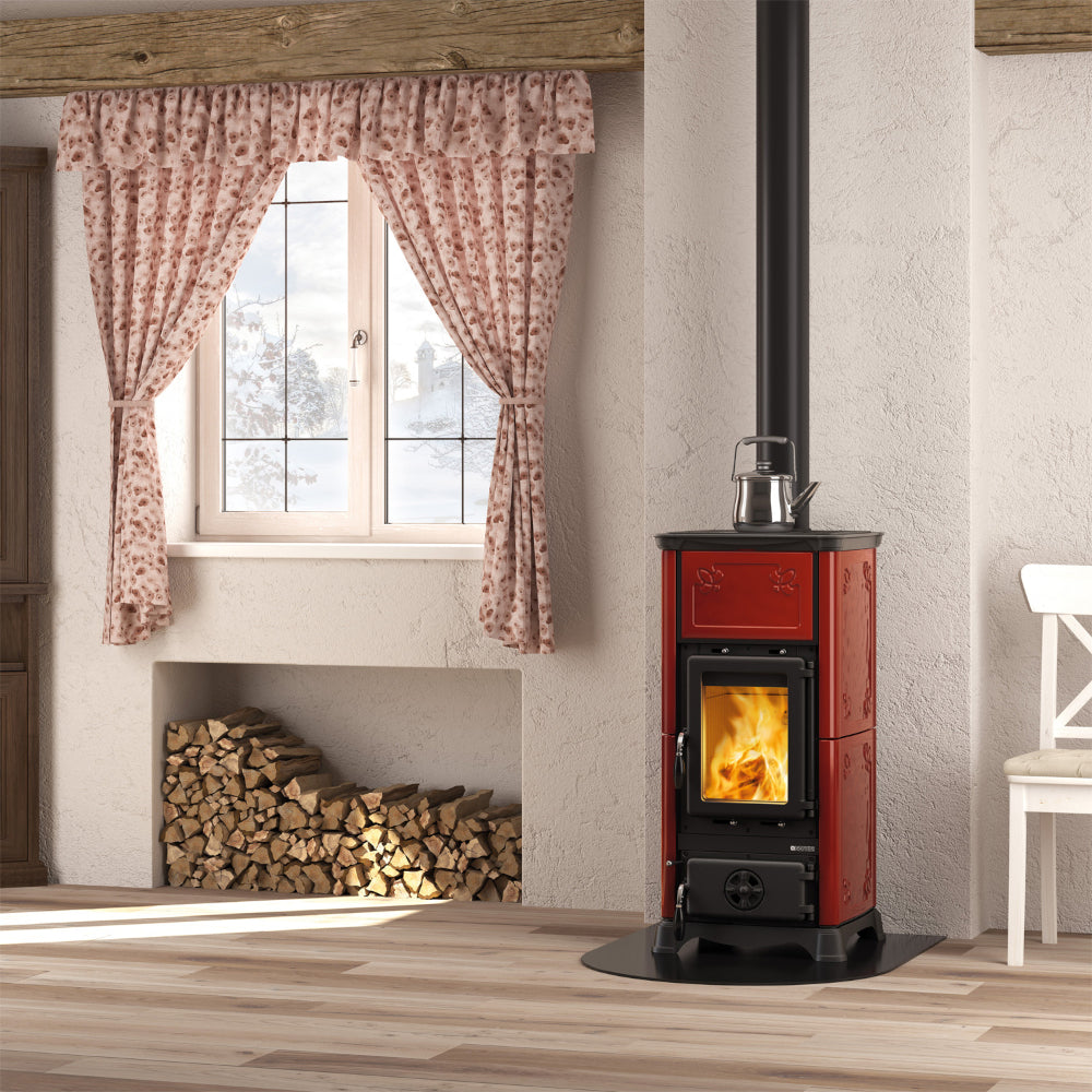 La Nordica Kaminofen EMILIANA.16 in Bordeaux mit Beispiel Flammenbild in gemuetlichem Zimmer | Klimaworld.com