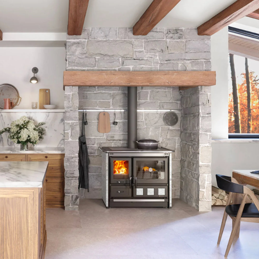 Ambientebild: La Nordica Kuechenofen Rosa.16 XXL, vor Steinwand mit Holzdecke, Feuerraum links, Backofen rechts | Klimaworld.com