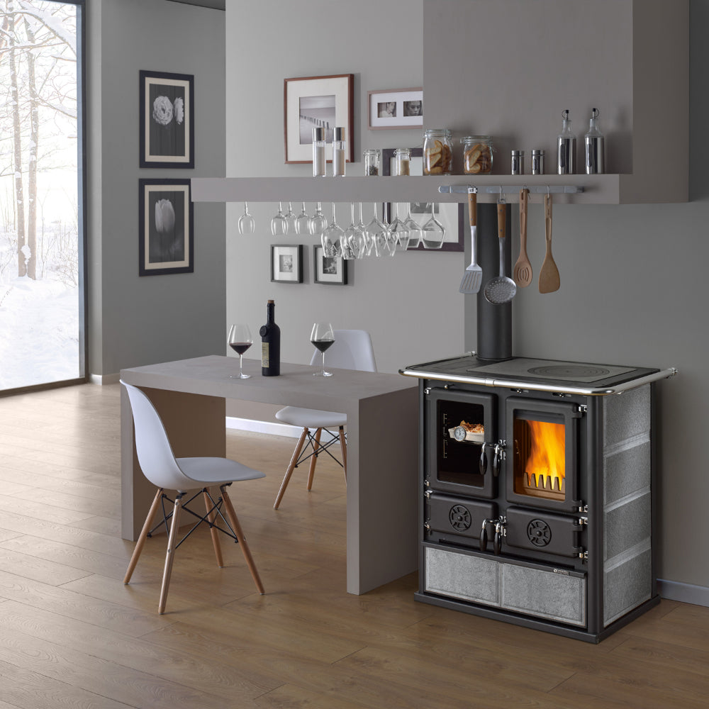 Ambientebild: La Nordica Kuechenofen ROSETTA SX.16 Petra freistehend, Naturstein-Seiten, schwarze Front, Feuer sichtbar, heller moderner Raum | Klimaworld.com