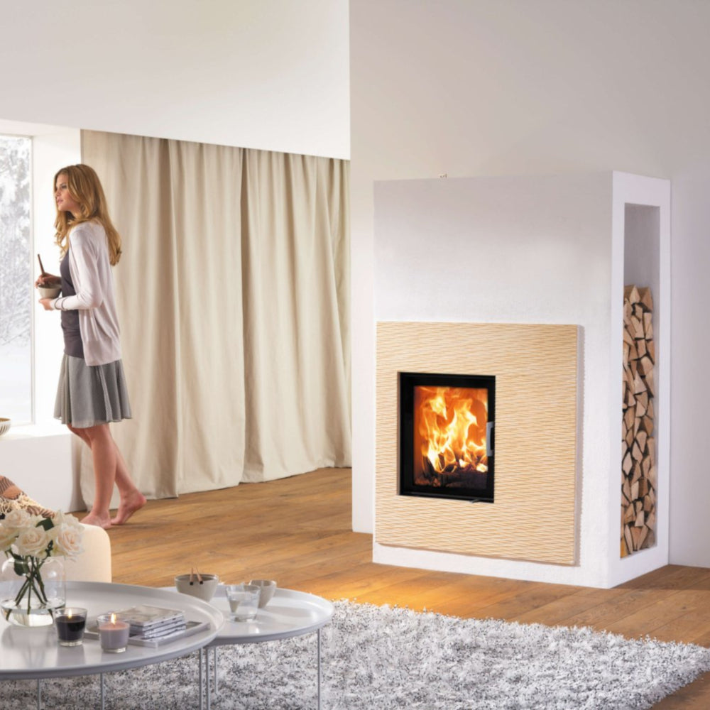 Kera Xtra 45 Kamineinsatz brennend, weisse Umrahmung, Holzfach rechts, Wohnzimmer mit Vorhang und Tisch | klimaworld.com