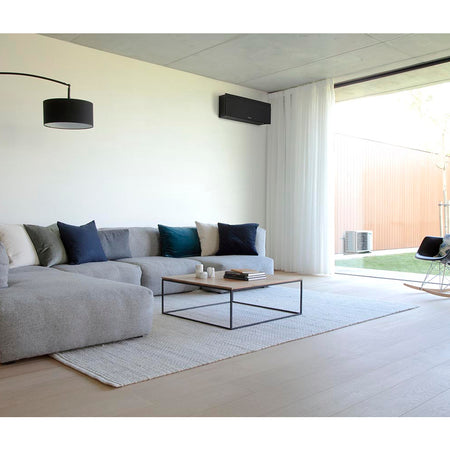 Daikin Emura 3 Wandgeraet in mattschwarz, schlankes Gehaeuse hoch an heller Wohnzimmerwand ueber Sofa | Klimaworld.com
