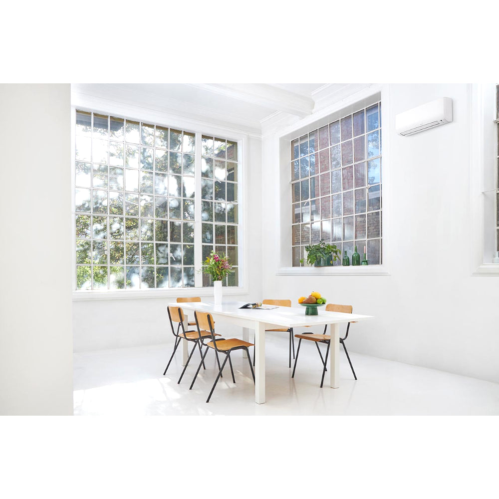Ambientebild: Daikin Comfora Wandgeraet hoch an weisser Wand in hellem Esszimmer mit Tisch, Stuehlen und grossen Fenstern | Klimaworld.com